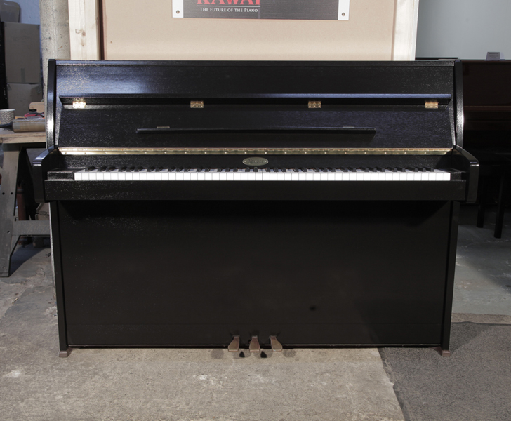 Pre-owned, 1995, Kemble upright piano with a black polished case and brass fittings. Piano has an eighty-eight note keyboard and three pedals.